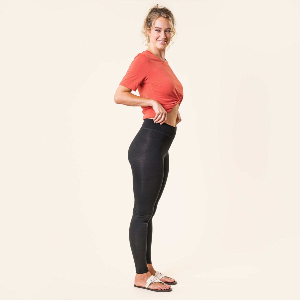 Woman wearing a red crop top and black organic cotton leggings on a plain background