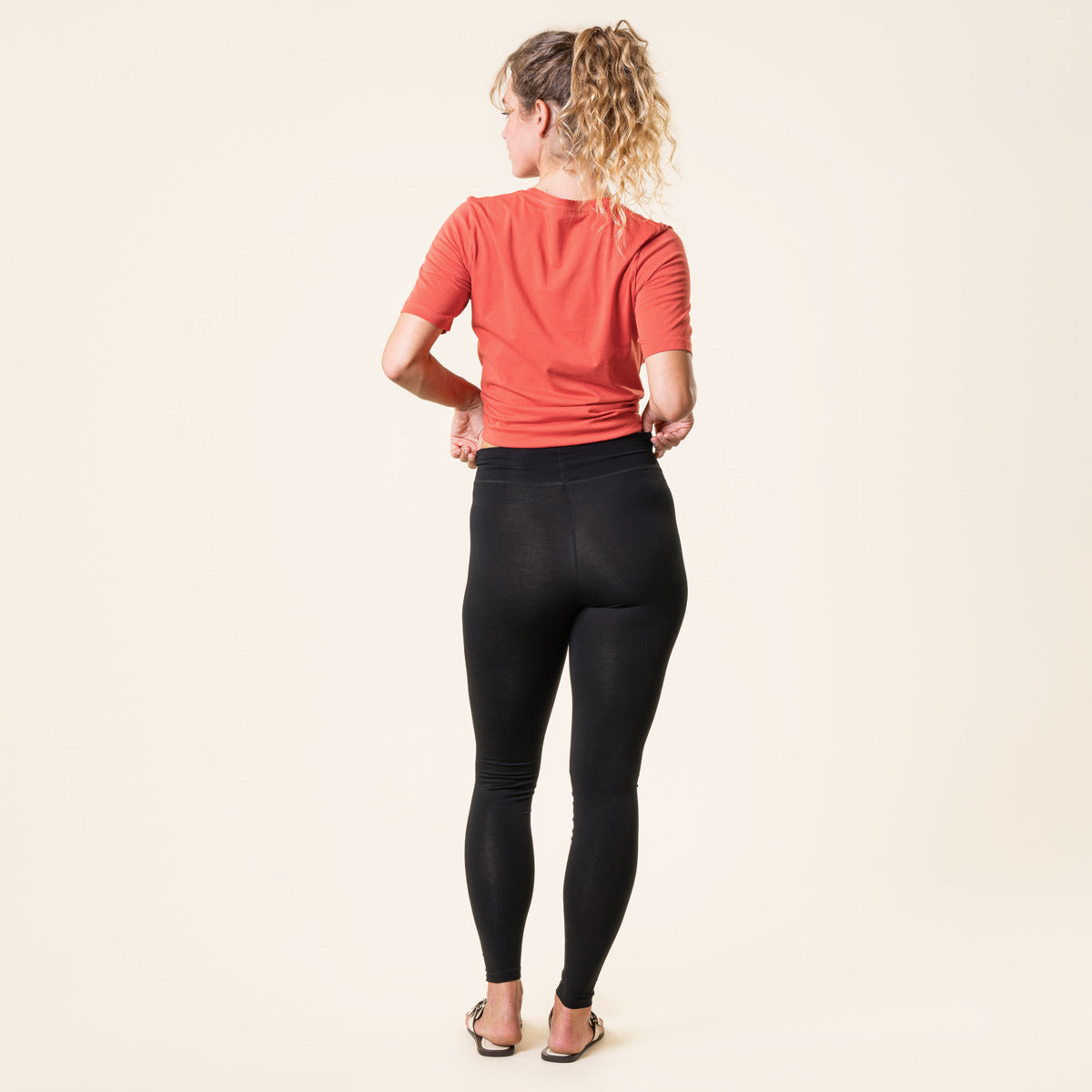 Person wearing a red shirt and black organic cotton leggings on a beige background
